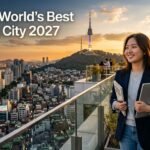 A smiling female student holding a laptop and books on a rooftop terrace overlooking the Seoul skyline and Namsan Seoul Tower at sunset, with text reading "Seoul – World’s Best Student City 2027."